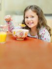 Retrato chica sonriente comiendo cereal en la mesa del desayuno - foto de stock