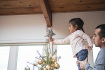 Father lifting toddler girl putting star on Christmas tree — Stock Photo
