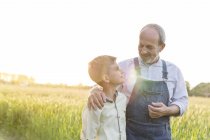 Abuelo agricultor y nieto abrazándose en campo de trigo rural - foto de stock