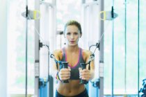 Mujer enfocada usando equipo de ejercicio por cable en el gimnasio - foto de stock