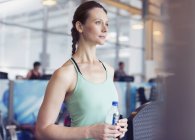 Pensive woman drinking water at gym — Stock Photo