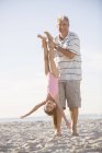 Older man playing with granddaughter on beach — Stock Photo