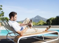 Man using digital tablet on lounge chair at poolside — Stock Photo