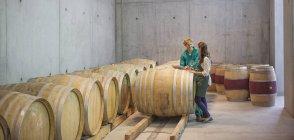 Vintners talking at barrels in winery cellar — Stock Photo