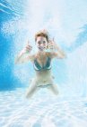 Woman giving thumbs up underwater in swimming pool — Stock Photo