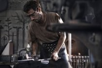 Blacksmith hammering iron at anvil in forge — Stock Photo