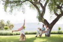 Casal assistindo filha fazer cartwheel ao ar livre — Fotografia de Stock