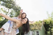 Carefree mother piggybacking daughter with arms outstretched in backyard — Stock Photo