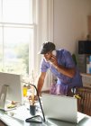 Uomo che parla al telefono e usa il computer alla scrivania nel soleggiato ufficio di casa — Foto stock
