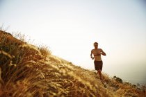 Hombre de pecho desnudo corriendo en la ladera soleada - foto de stock