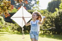 Begeistertes Mädchen läuft mit Drachen im sonnigen Garten — Stockfoto