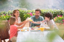 Familie prostet Orangensaftgläser am Tisch im Garten zu — Stockfoto
