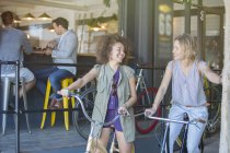 Smiling women on bicycles outside cafe patio — Stock Photo