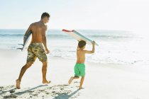 Père et fils portant planche de surf et bodyboard sur la plage — Photo de stock
