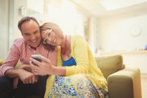 Smiling mature couple texting with cell phone in living room — Stock Photo