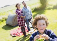 Portrait smiling boy eating hamburger with parents at sunny campsite — Stock Photo