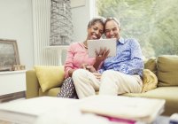 Sorrindo casal maduro usando tablet digital no sofá da sala de estar — Fotografia de Stock
