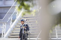 Businessman in suit and helmet carrying bicycle down urban stairs — Stock Photo