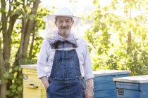 Retrato apicultor confiante em chapéu protetor ao lado de colmeias — Fotografia de Stock