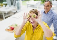 Portrait playful mature woman covering eyes with kiwi slices — Stock Photo