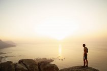 Coureur sur rochers regardant coucher de soleil vue sur l'océan — Photo de stock