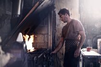 Blacksmith working at fire in forge — Stock Photo