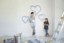 Madre e hija pintando corazones azules en la pared - foto de stock
