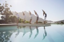 Jeunes gens attrayants pratiquant le yoga au bord de la piscine — Photo de stock