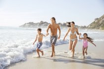 Family running together in waves — Stock Photo