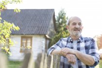 Selbstbewusster Bauer lehnt an Zaun vor Bauernhaus — Stockfoto