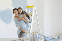 Retrato de madre e hija abrazándose cerca de materiales de pintura - foto de stock