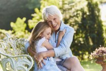 Grandmother and granddaughter hugging on garden bench — Stock Photo
