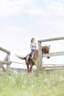Woman horseback riding in fenced rural pasture — Stock Photo