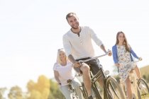 Улыбающийся молодой человек катается на велосипеде с женщинами — стоковое фото