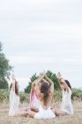 Boho women meditating with hands clasped overhead in circle in rural field — Stock Photo