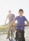 Pai e filho andando de bicicleta na praia ensolarada — Fotografia de Stock
