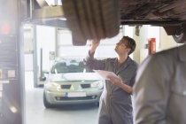Mechaniker mit Klemmbrett unter Auto in Autowerkstatt — Stockfoto
