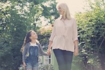 Großmutter und Enkelin halten sich an Händen und gehen im Garten spazieren — Stockfoto