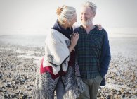 Senior couple hugging and walking on sunny rocky beach — Stock Photo