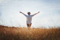 Exuberant senior woman with arms outstretched in sunny field — Stock Photo