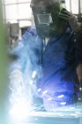 Сварщик в защитной рабочей одежде работает на заводе — стоковое фото