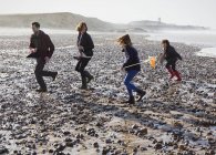 Família correndo na praia rochosa — Fotografia de Stock