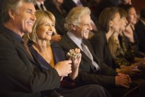 Smiling couple holding opera glasses in theater audience — Stock Photo