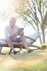 Старший чоловік використовує цифровий планшет на кріслі для відпочинку на задньому дворі — стокове фото