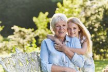Портрет усміхнена бабуся і онука обіймаються в саду — стокове фото