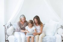 Multi-generation women using digital tablet on daybed — Stock Photo