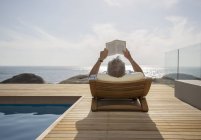 Hombre mayor leyendo junto a la piscina - foto de stock