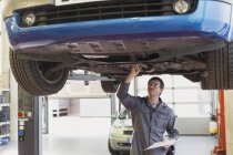 Mechaniker mit Klemmbrett arbeitet unter Auto in Autowerkstatt — Stockfoto