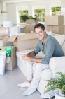 Portrait of smiling man enjoying coffee on sofa among cardboard boxes — Stock Photo