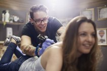 Tatuaje artista tatuar mujer de vuelta en el estudio - foto de stock